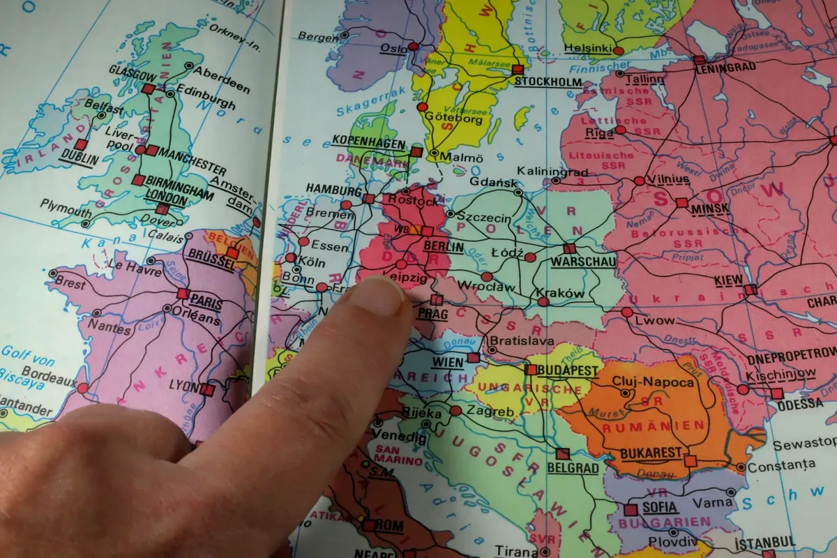 A finger points to Berlin on a colorful political map of Europe during the Cold War era.