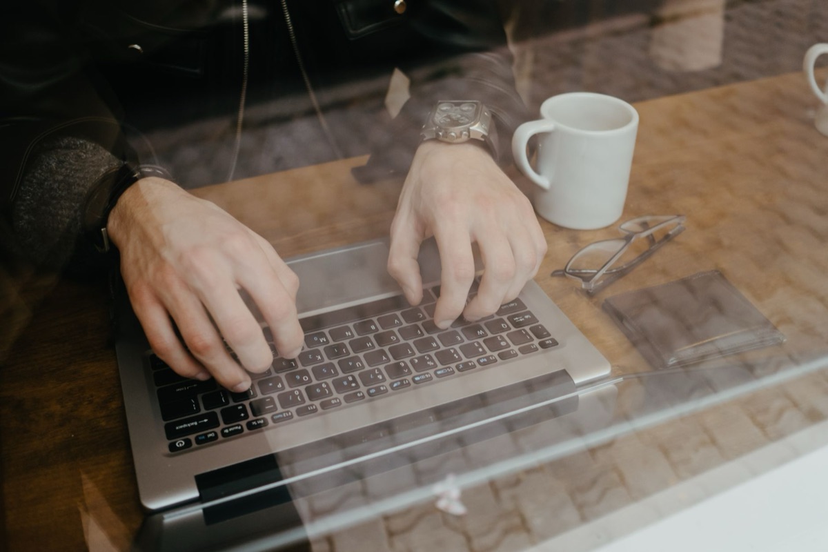 pessoa digitando no computador com xícara de café