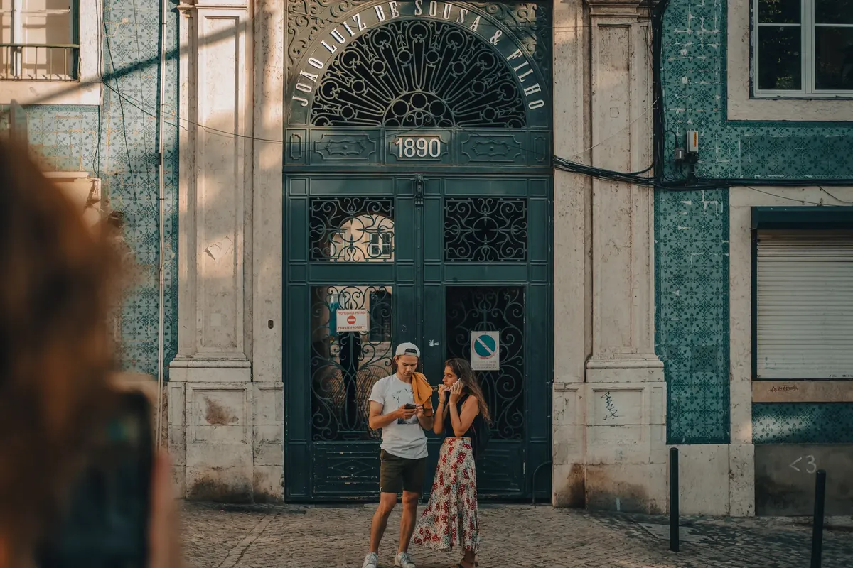 A couple stands by a traditional Portuguese facade in Lisbon, Portugal, enjoying a sunny day.