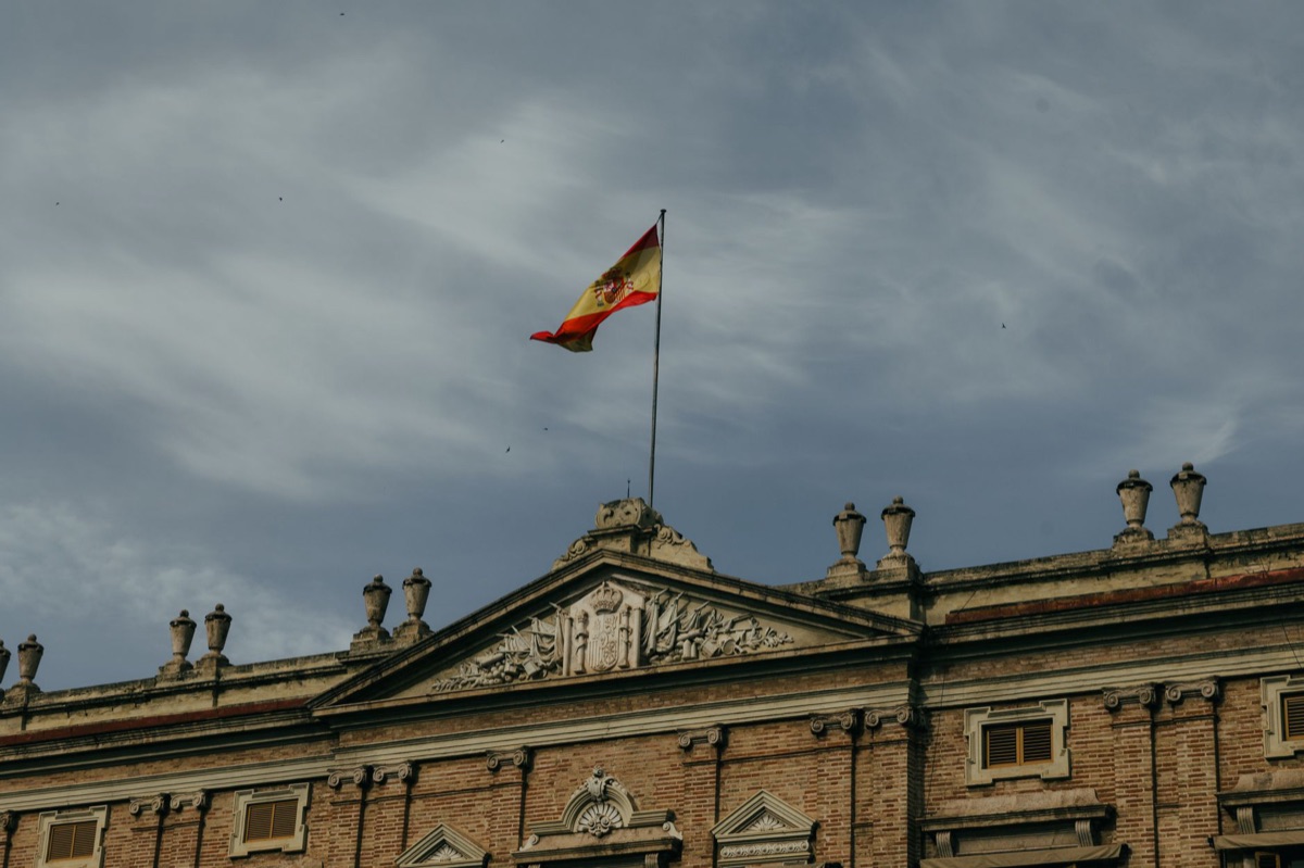 The Spanish flag waving against a beautiful Mediterranean coastline background